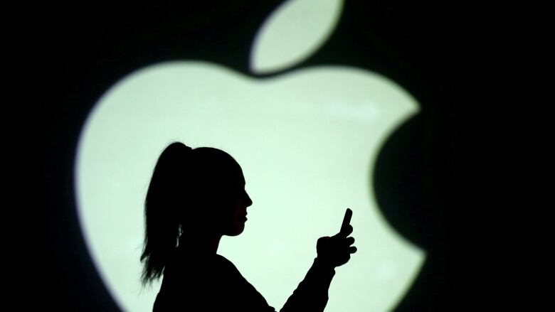 Silhouette of a mobile user seen next to a screen projection of the Apple logo