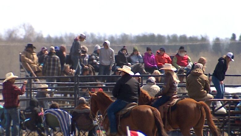 A crowd sits on bleachers and lawnchairs with two people on horses in the foreground.