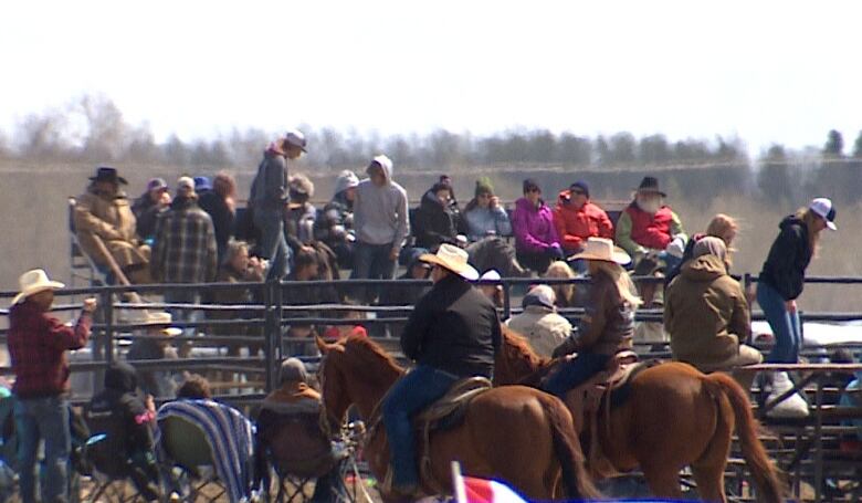 A crowd sits on bleachers and lawnchairs with two people on horses in the foreground.