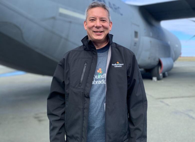 Man wearing a blue jacket standing in front of a plane.