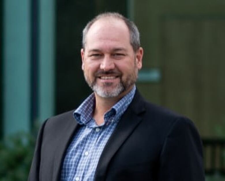 A bearded man wearing a jacket smiles for the camera. 