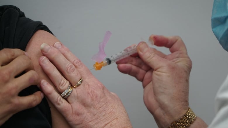 A close-up of a pharmacist's hands injecting a vaccine into a person's arm.