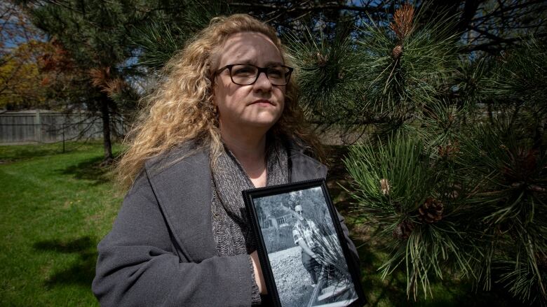 A woman holding a framed photograph of a man looks away from the camera for a photo.