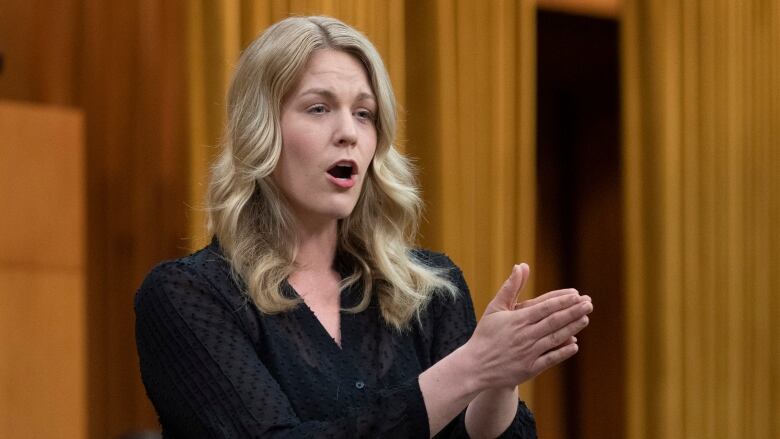 A woman in business wear gestures while speaking.