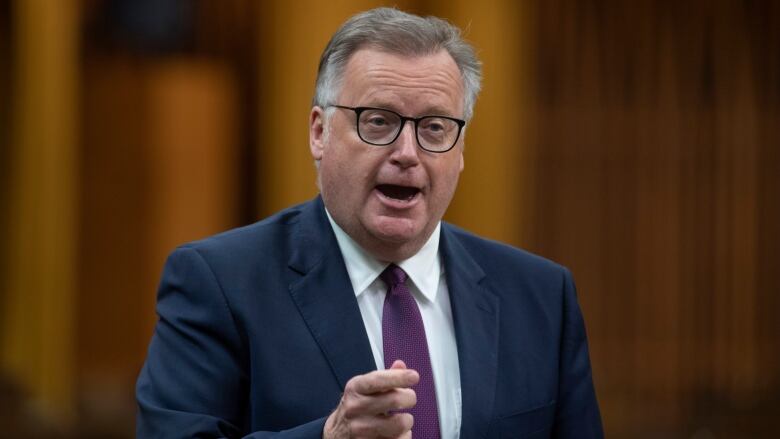 A man in a suit gestures while speaking.