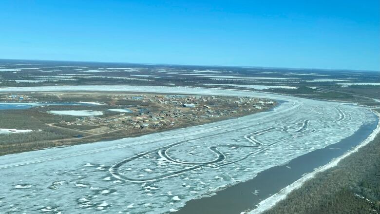 A small Arctic hamlet is seen from the air beside a partially ice-covered river.