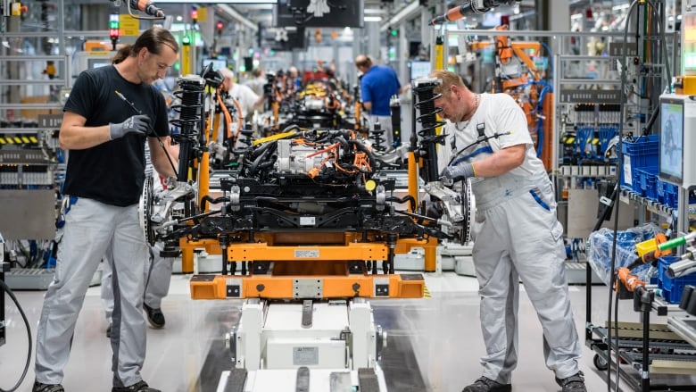 Two men assemble a car engine in a factory.