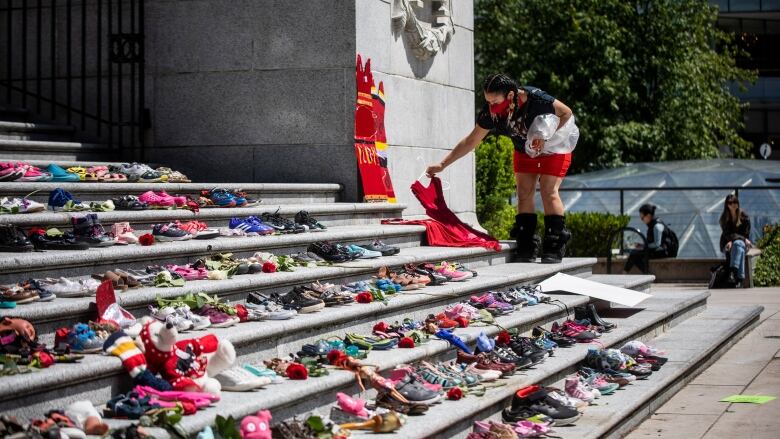 A woman lays a red dress on outdoor steps covered with shoes.