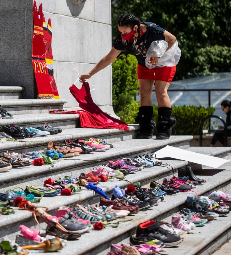 A woman lays a red dress on outdoor steps covered with shoes.