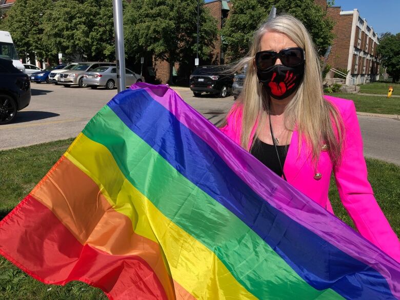 A woman wearing a black mask for COVID holds a rainbow pride flag