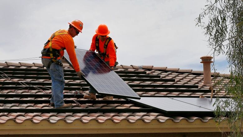 Construction workers install solar panels on the roof of a building.