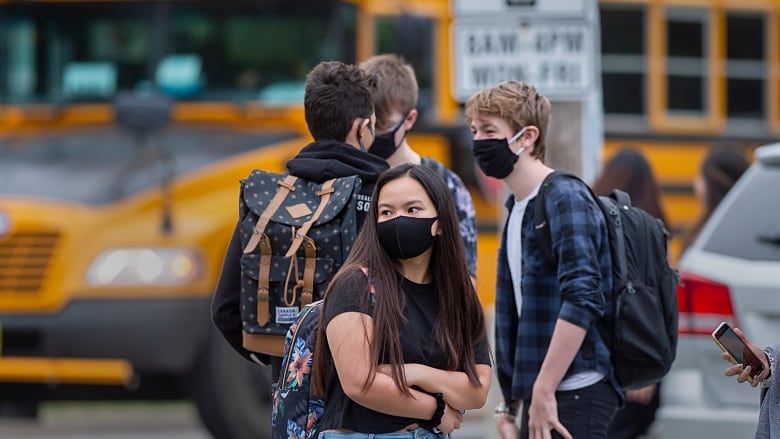 Students wearing masks stand in front of a bus.