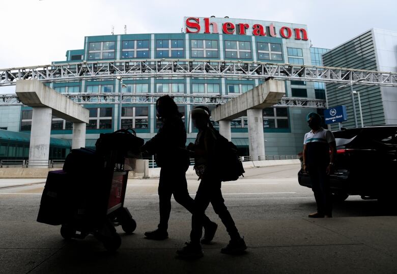 People walk with their luggage to travel to the United States during the COVID-19 pandemic in Toronto on Wednesday, June 9, 2021. 