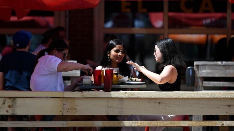 Three women wearing sunglasses sit on a patio. 