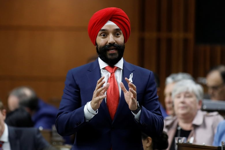 A man in a suit and red tie stands in the House of Commons.