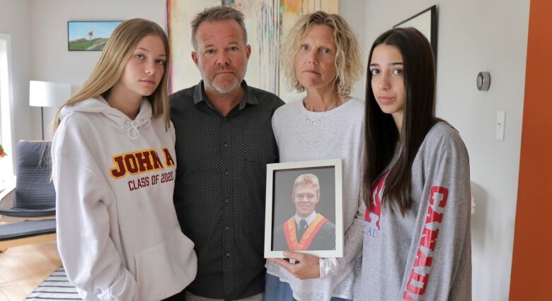 Four people stand together in a living room holding a graduation photo of a young man.