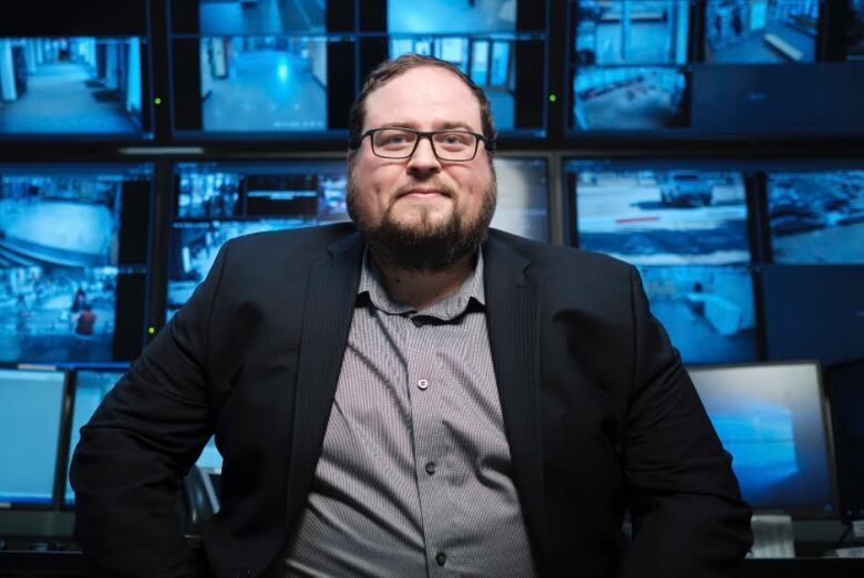 Man wearing a suit sits in front of computer monitors.