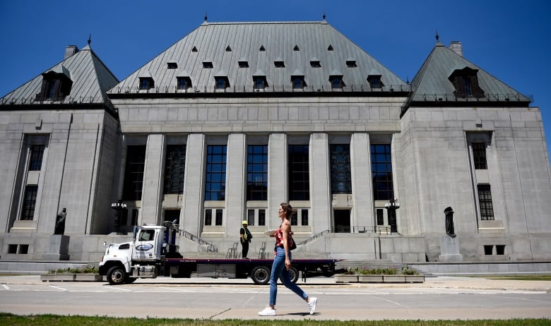 A woman walks in front of the Supreme Court of Canada on a sunny day