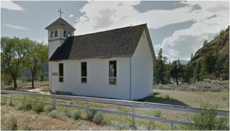 A white church surrounded by small trees and a white fence. 