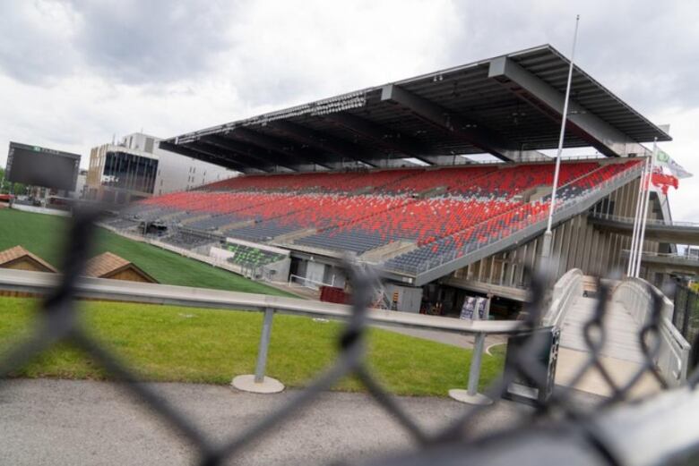 A stadium with red and grey seating photographed through a chainlink fence