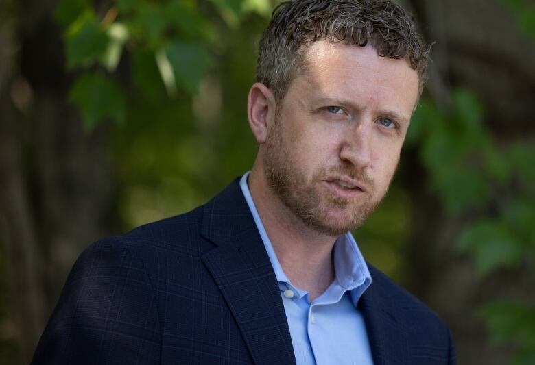 A white man with short, curly hair is wearing a navy suit