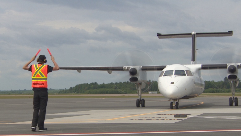 A plane sits on the tarmac with an employee in a high-vis vest standing in front of it.