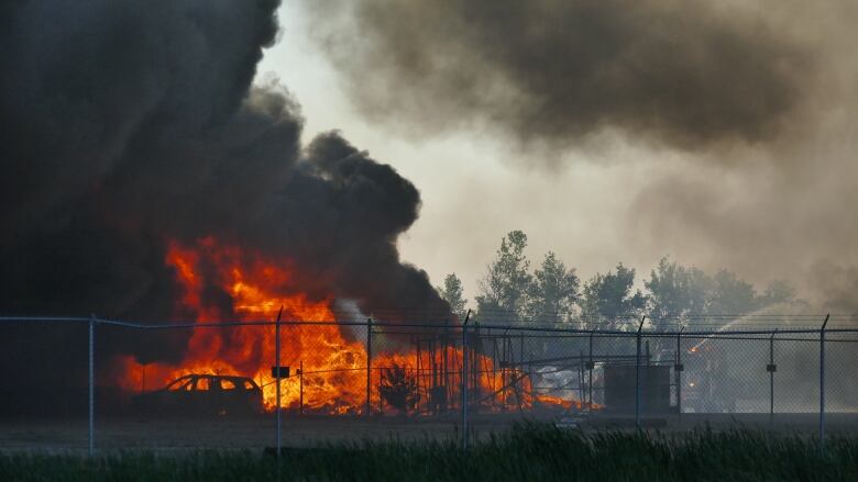 Flames and smoke are seen coming from behind a chain link fence.