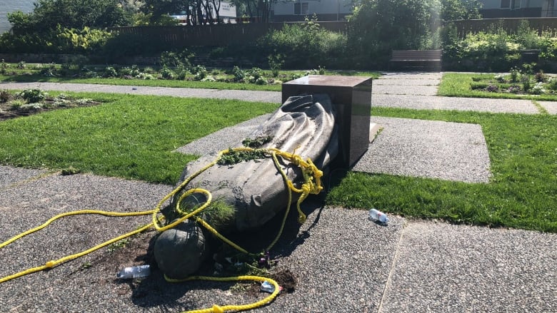 A statue lies face down with yellow ropes tied around it.