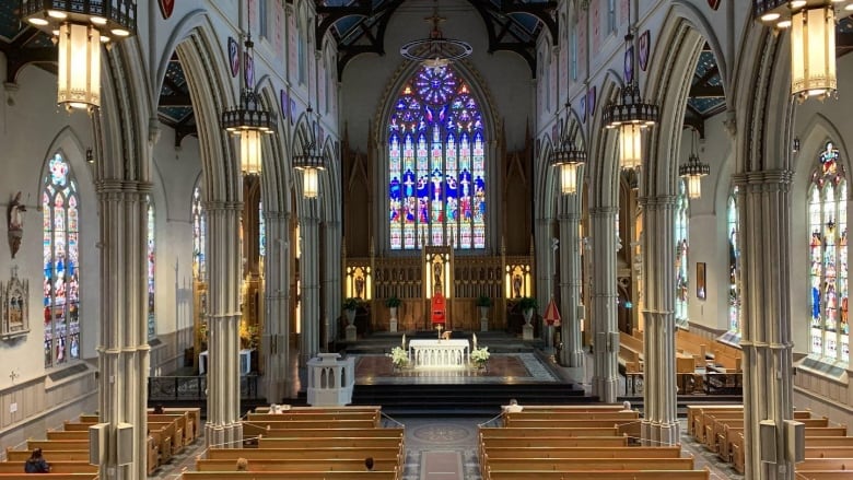 An interior photo of a cathedral shows tall arches, stained glass windows and church pews.