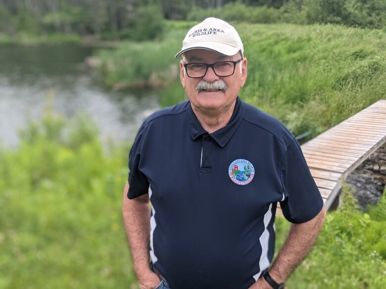 Man in golf shirt stands next to pond.