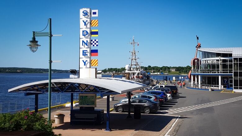 A parking lot and buildings are shown with a large vertical sign saying Sydney, with water in the background.