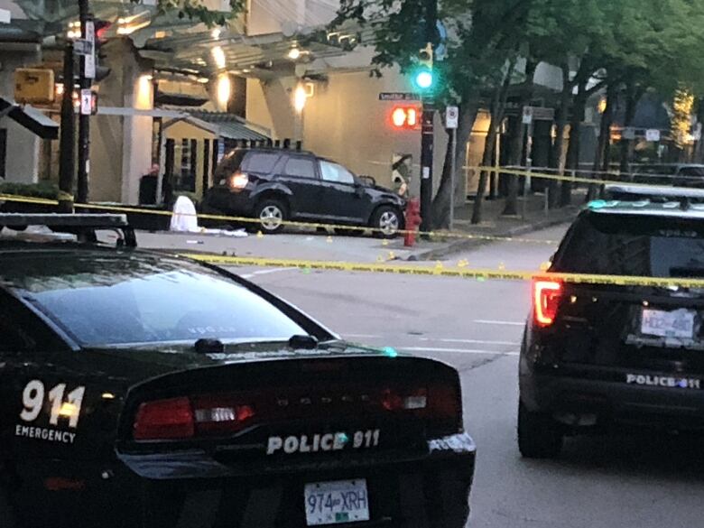 Two Vancouver police cars are in the foreground, with yellow police tape strung across the photo in multiple places. In the background a black SUV is seen on the sidewalk. It appears to show an airbag deployed inside the passenger window.