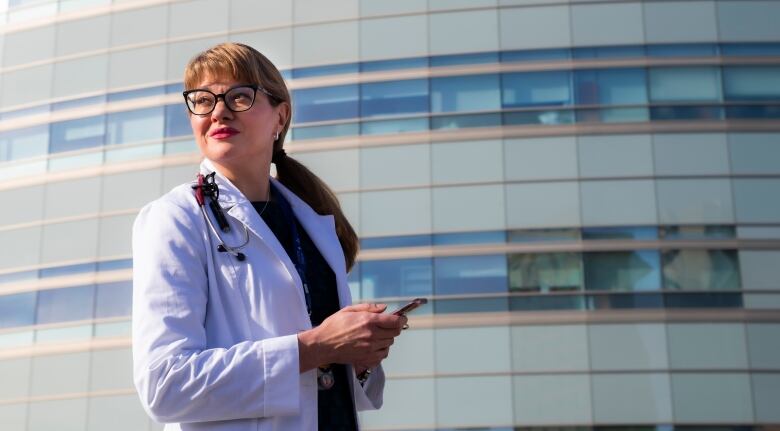 Woman stands with a smartphone in her hand looking away from the camera.