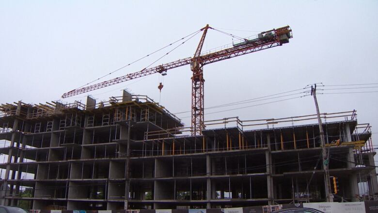 A yellow construction crane in front of a high rise building under construction. 