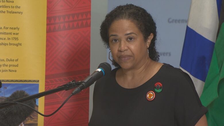 A Black woman with dark curly hair is standing in front of a mic on a podium