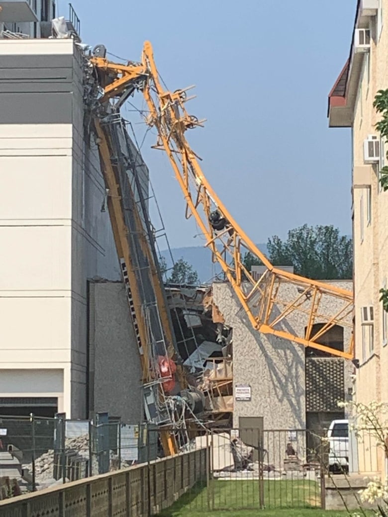 A yellow crane lies crashed into an office building.