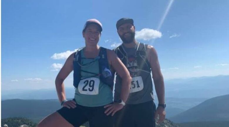 A couple wearing hiking gear, backpacks and bibs with numbers on them are pictured after exercising on a sunny day.