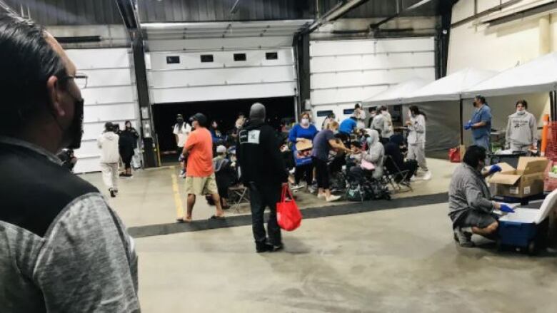 A number of people gathered in an airport hanger, with some emergency supplies in the background.