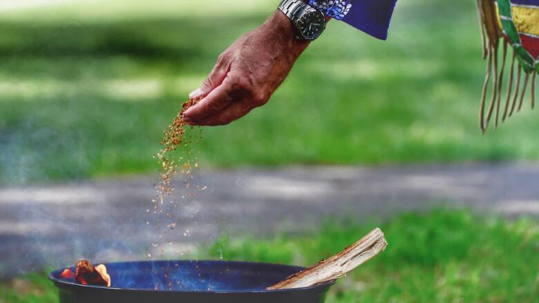 An Indigenous man's hand feeds material into a ceremonial fire.