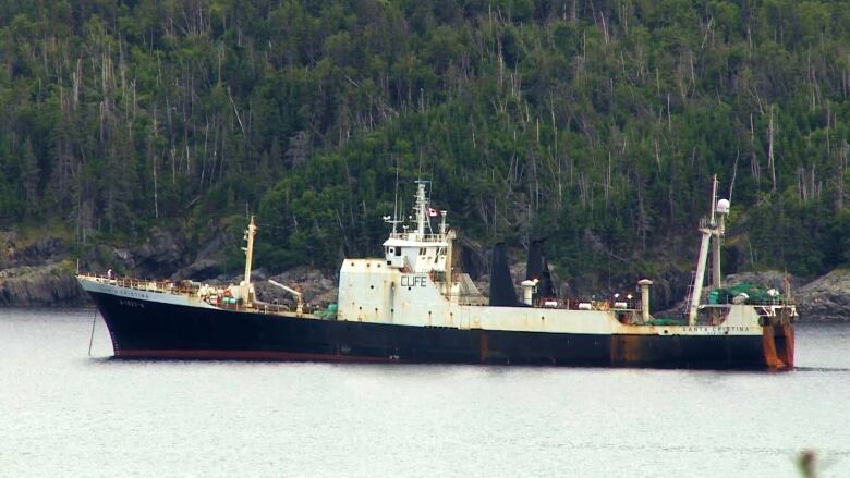 A fishing vessel sits anchored on the water near land.