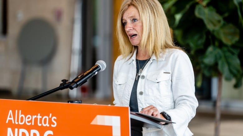 A woman making a speech stands at a podium with an orange placard in the front.