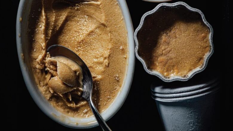 overhead shot of 2 grey containers of coffee-flavoured kulfi, with a spoon in one of them, sitting on a black surface