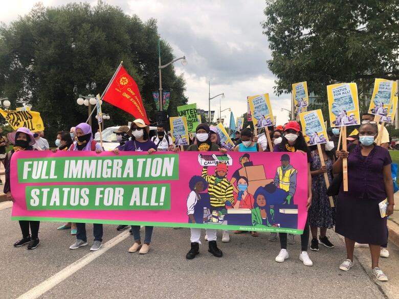 A group of people standing in a street hold placards and march behind a sign reading 