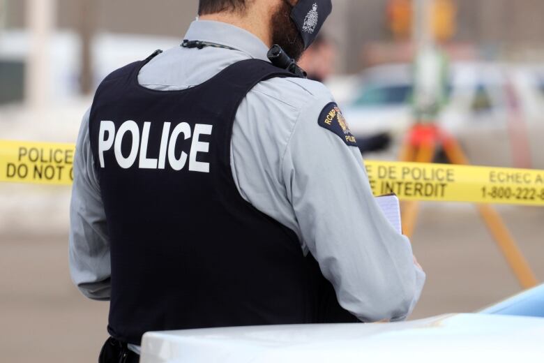 A police officer wears a vest that says police in front of crime scene tape.