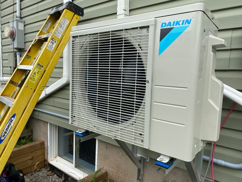 A heat pump on the outside of a house with a yellow ladder next to it