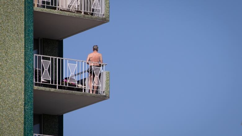 A shirtless man stands on his balcony in Vancouver.