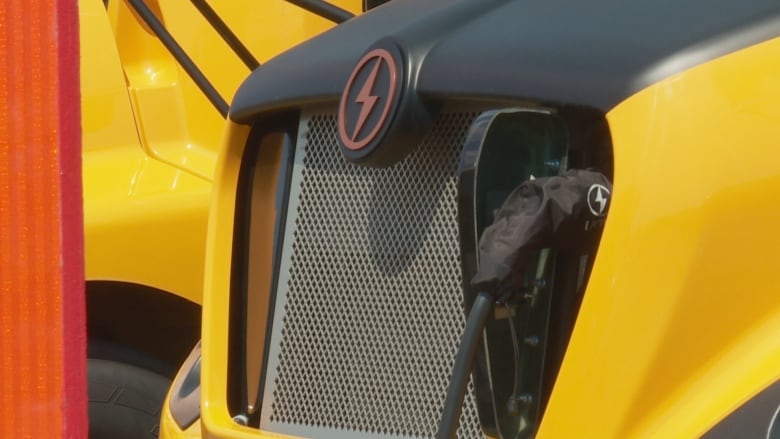 A close up shows a charger plugged in to an electric school bus.