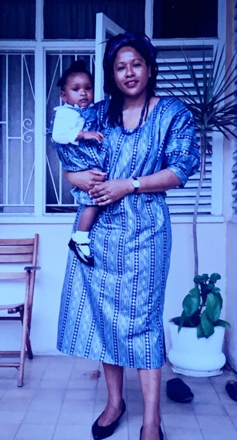 A Black woman wearing a blue dress holding a Black baby