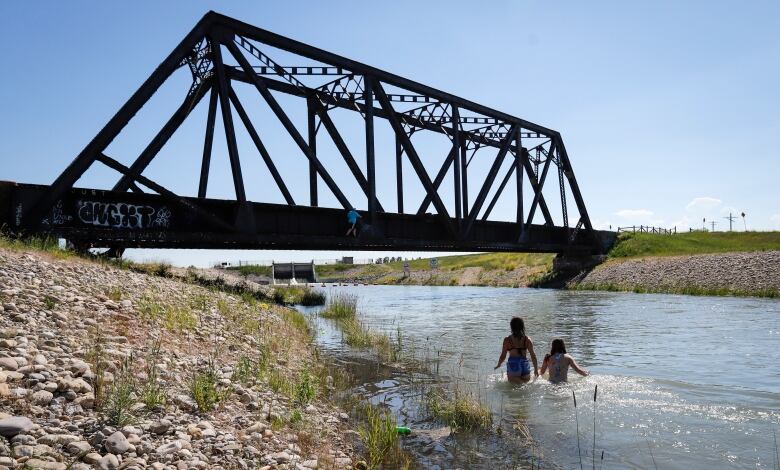 2 teens swim in a river near a bridge. 