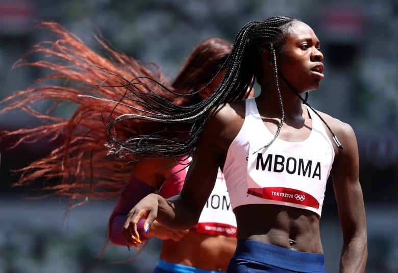 A Black woman in athletic wear look to her left, her braids blowing in the wind. 